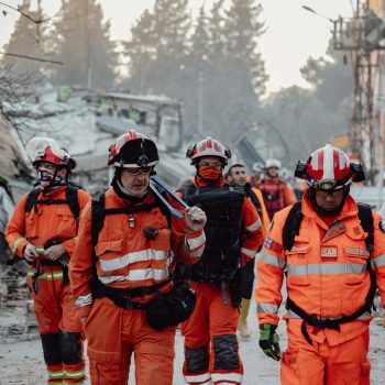 Search and rescue team in orange uniforms in a demolished area, assessing damage and carrying out operations.